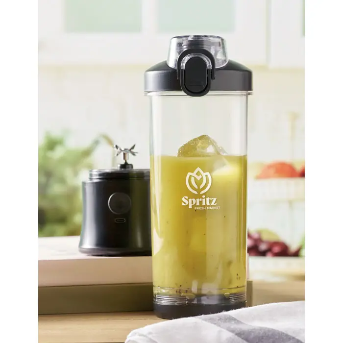 Vaso de batido amarillo con hielo en una licuadora portátil Spritz Fresh Market sobre encimera de cocina.