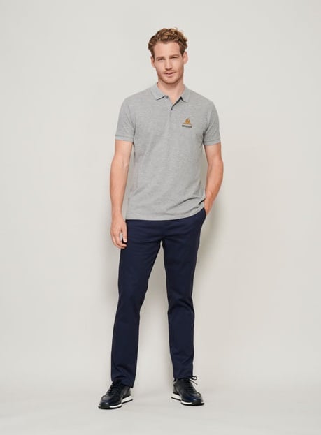 Hombre con polo gris de manga corta y pantalón azul marino con zapatillas negras.