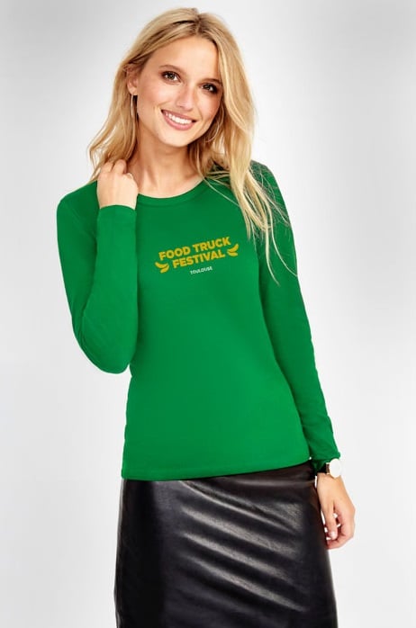 Mujer con camiseta verde de manga larga con texto amarillo "Food Truck Festival Toulouse" y falda negra de cuero.