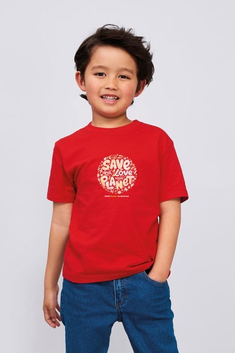 Niño con camiseta roja de algodón con mensaje ecológico blanco y pantalón vaquero azul.