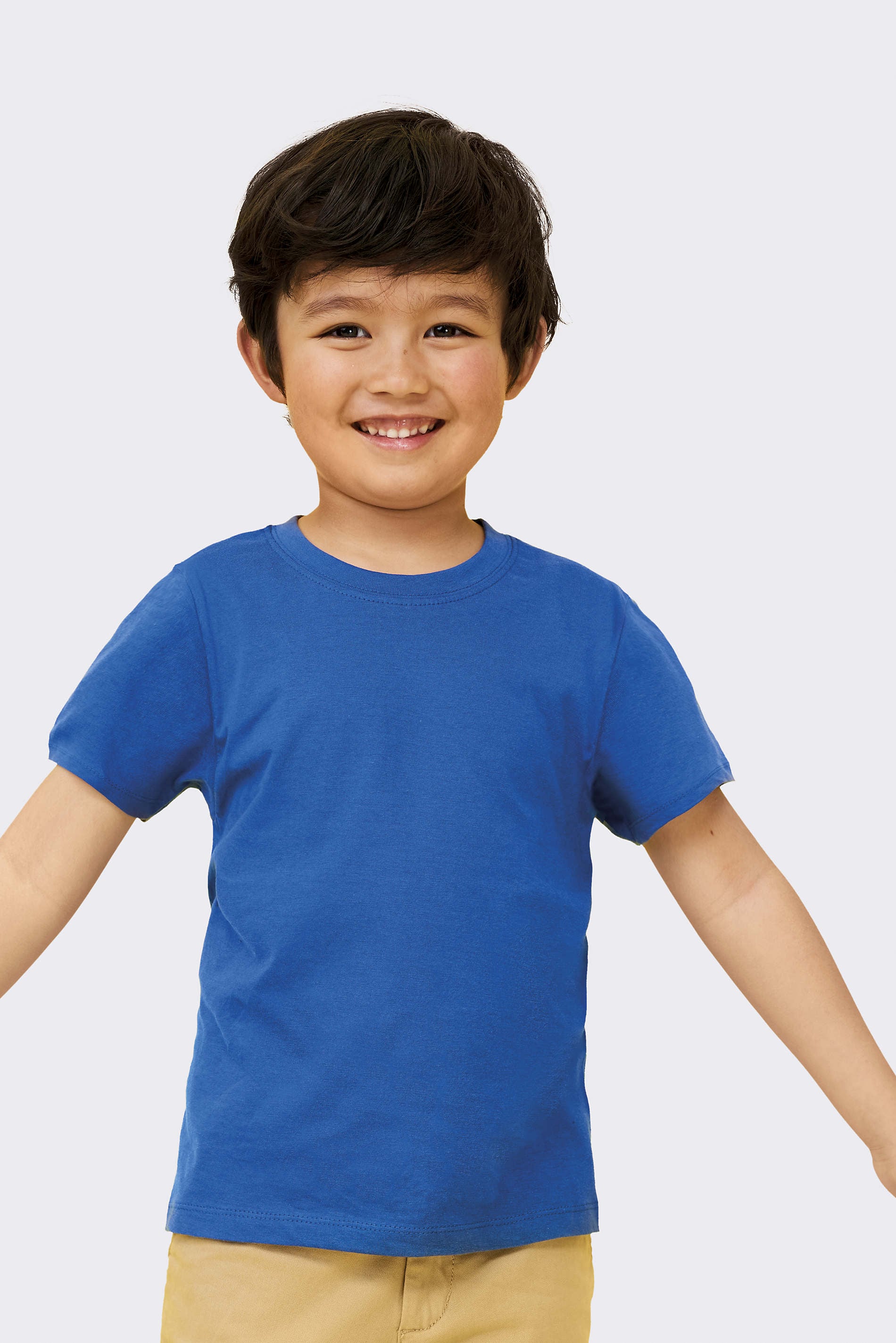 Niño sonriente con camiseta azul de algodón y pantalón beige.