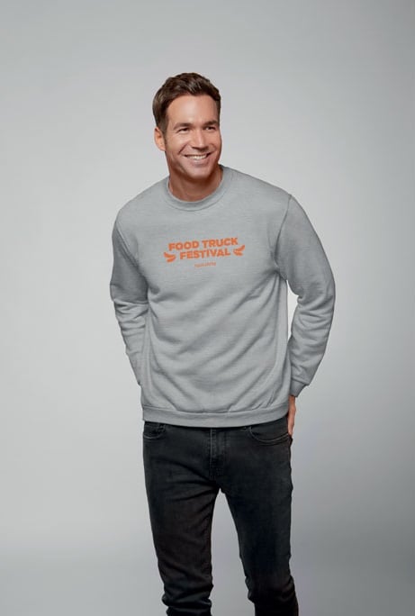Hombre con sudadera gris claro con texto naranja "Food Truck Festival" y pantalones vaqueros negros.