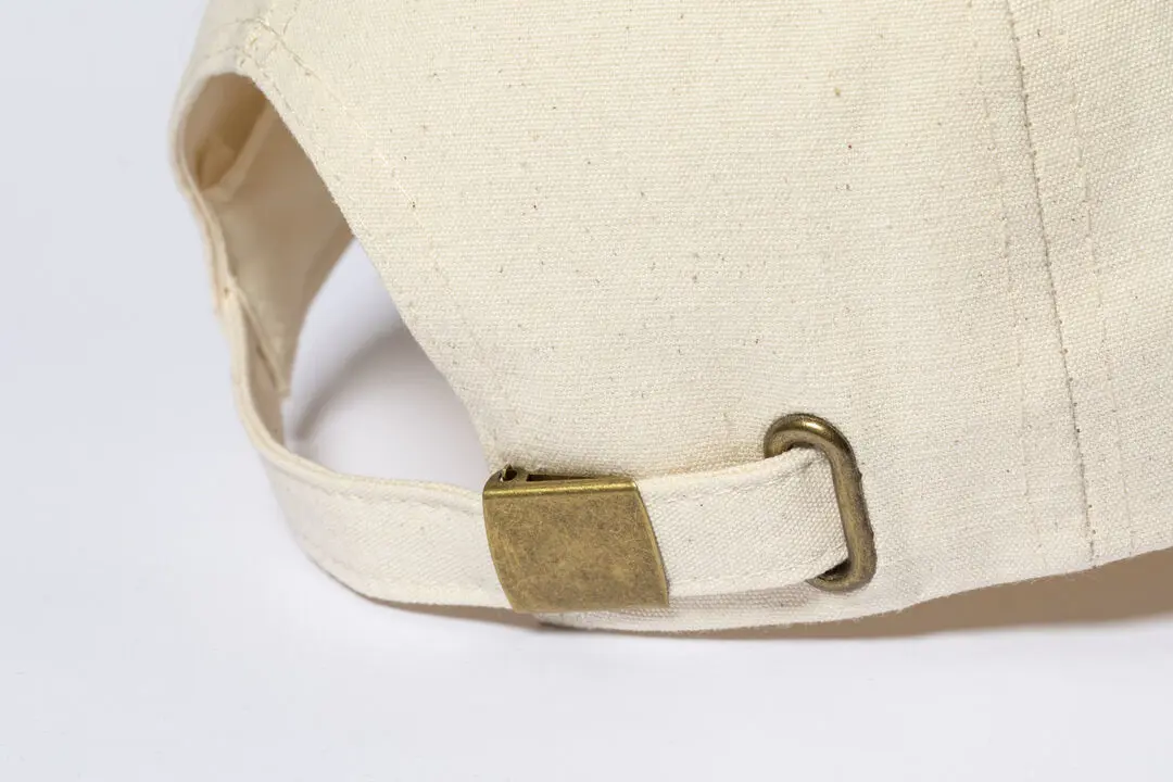 Cierre trasero de hebilla metálica en gorra de tela beige.