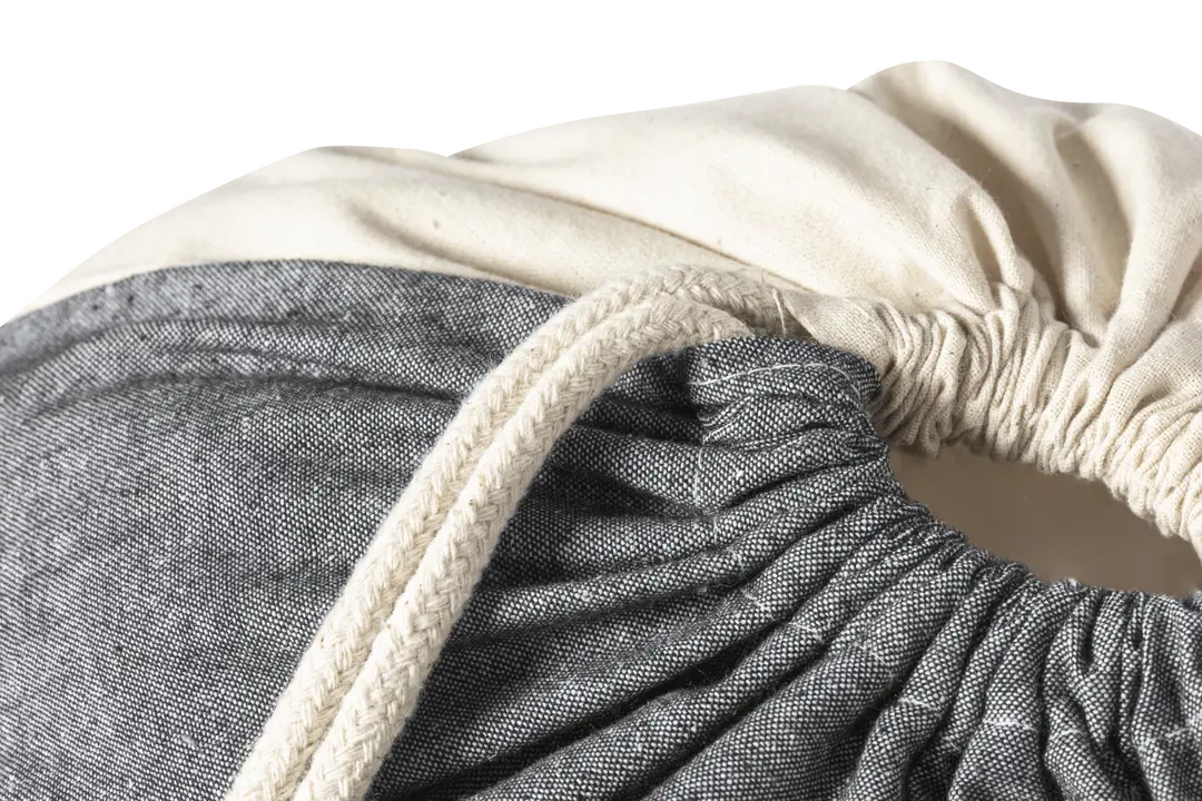 Bolsa de tela con cierre de cordón trenzado en colores gris y beige.