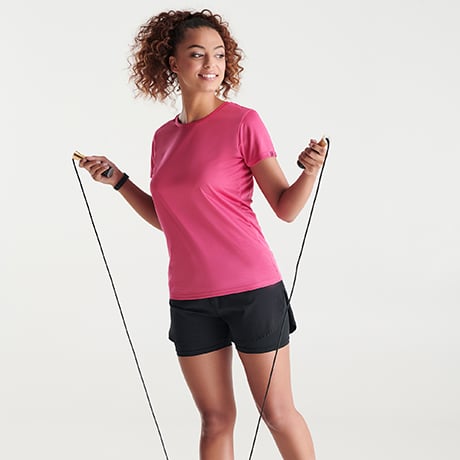 Mujer con camiseta rosa y pantalones cortos negros saltando a la comba.