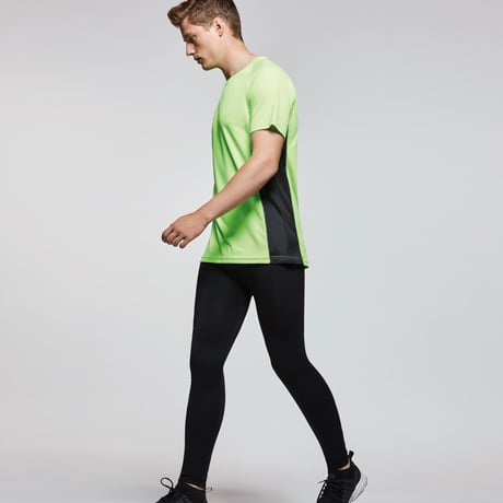 Hombre con camiseta deportiva verde y negra y mallas negras caminando.