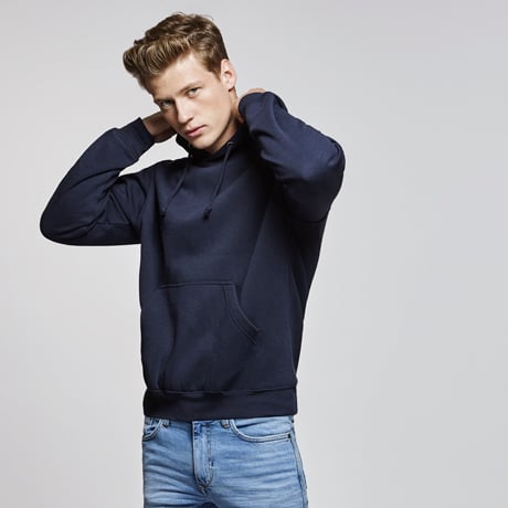 Hombre joven con sudadera azul marino con capucha y bolsillo frontal combinado con vaqueros claros.