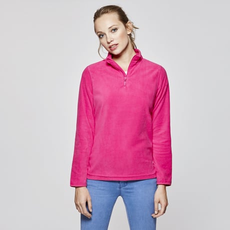 Jersey de forro polar rosa con cremallera corta y cuello alzado, combinado con vaqueros azules.