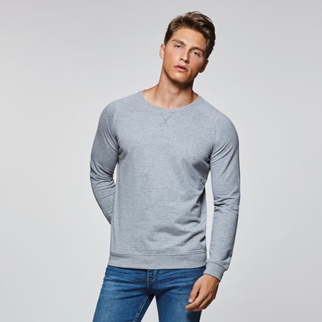 Hombre con sudadera gris de manga larga y cuello redondo combinada con vaqueros azules.