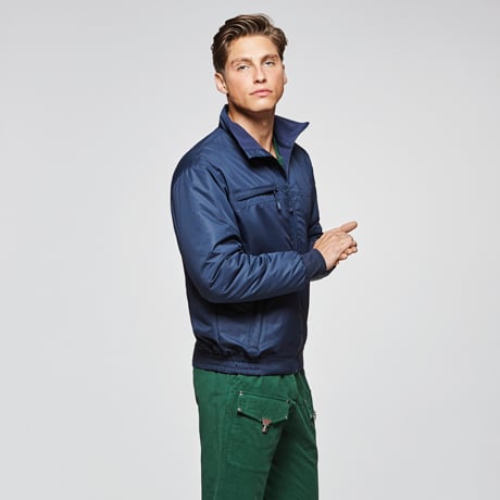 Hombre con chaqueta azul marino de tejido técnico y pantalones verdes con bolsillos laterales.