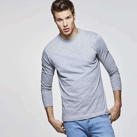 Hombre joven con camiseta gris de manga larga y pantalones vaqueros azules.