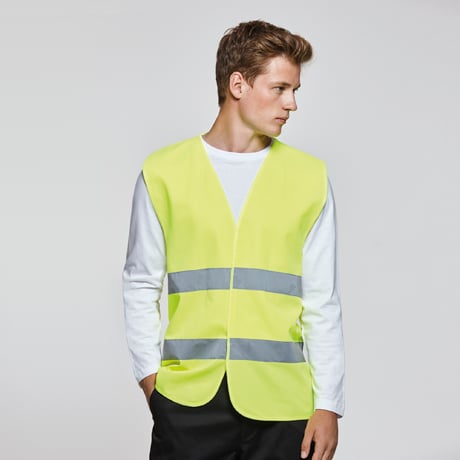 Chaleco reflectante amarillo con franjas grises sobre camiseta blanca y pantalón negro.