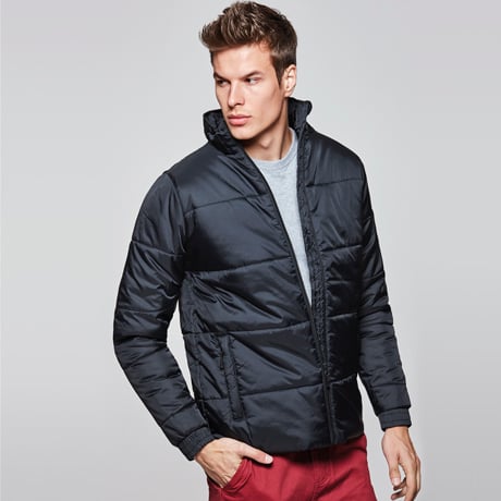 Chaqueta acolchada negra con cremallera y cuello alto, combinada con camiseta gris y pantalones rojos.