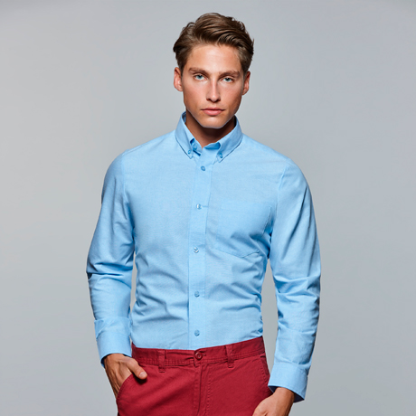 Hombre con camisa azul celeste de manga larga y pantalones rojos.