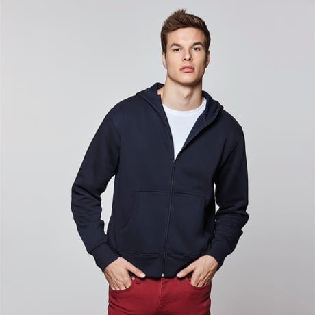 Hombre con sudadera azul marino con cremallera y capucha sobre camiseta blanca y pantalones rojos.