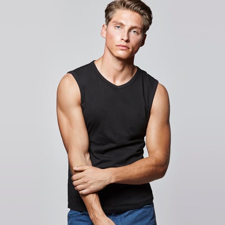 Hombre con camiseta sin mangas negra de algodón ajustada y pantalones azules.