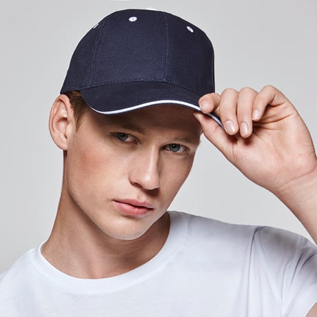 Hombre joven con gorra azul marino de visera curva y camiseta blanca.
