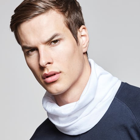 Hombre joven con cuello tubular blanco sobre camiseta azul marino.