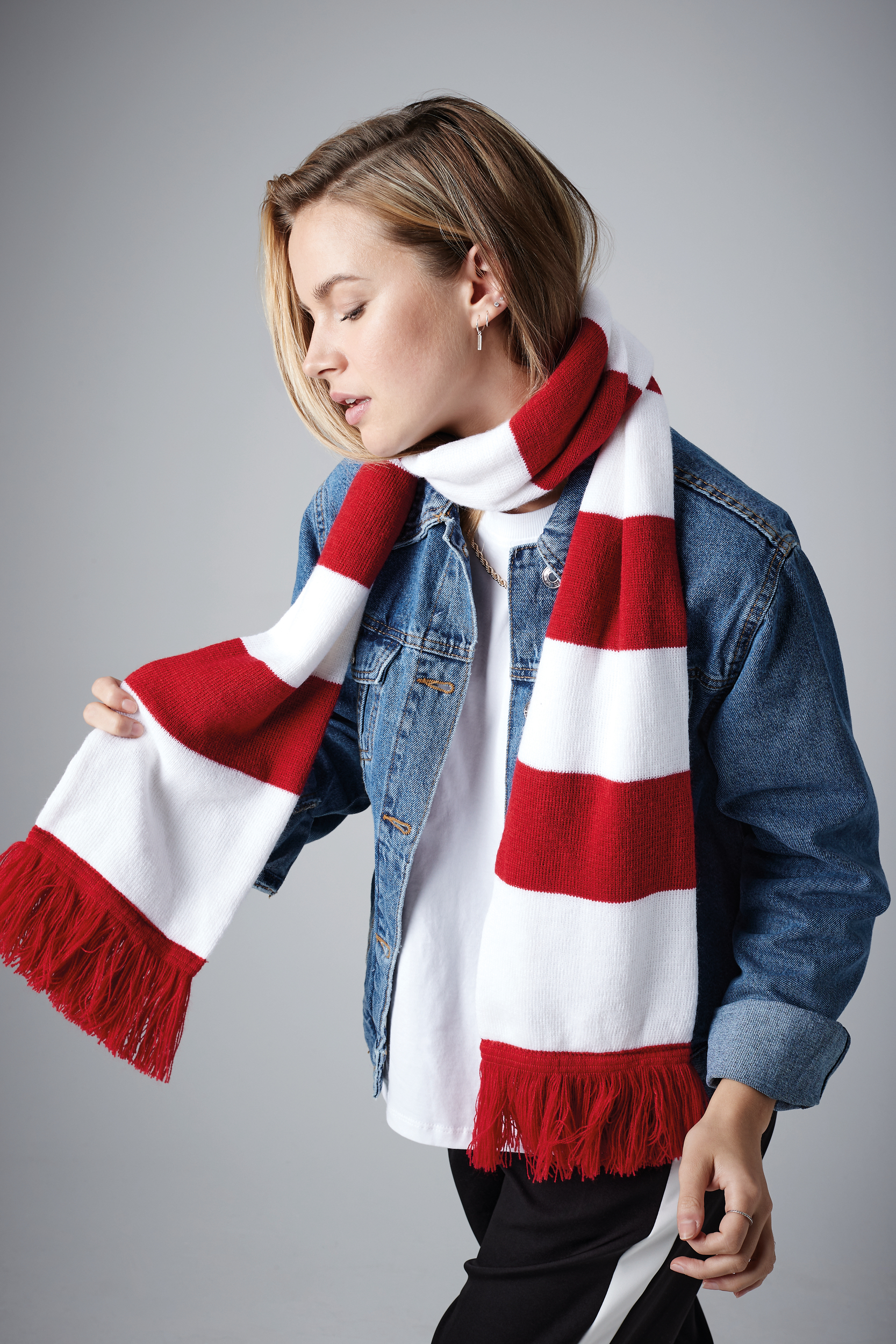 Mujer con bufanda de rayas rojas y blancas de punto con flecos, chaqueta vaquera y camiseta blanca.