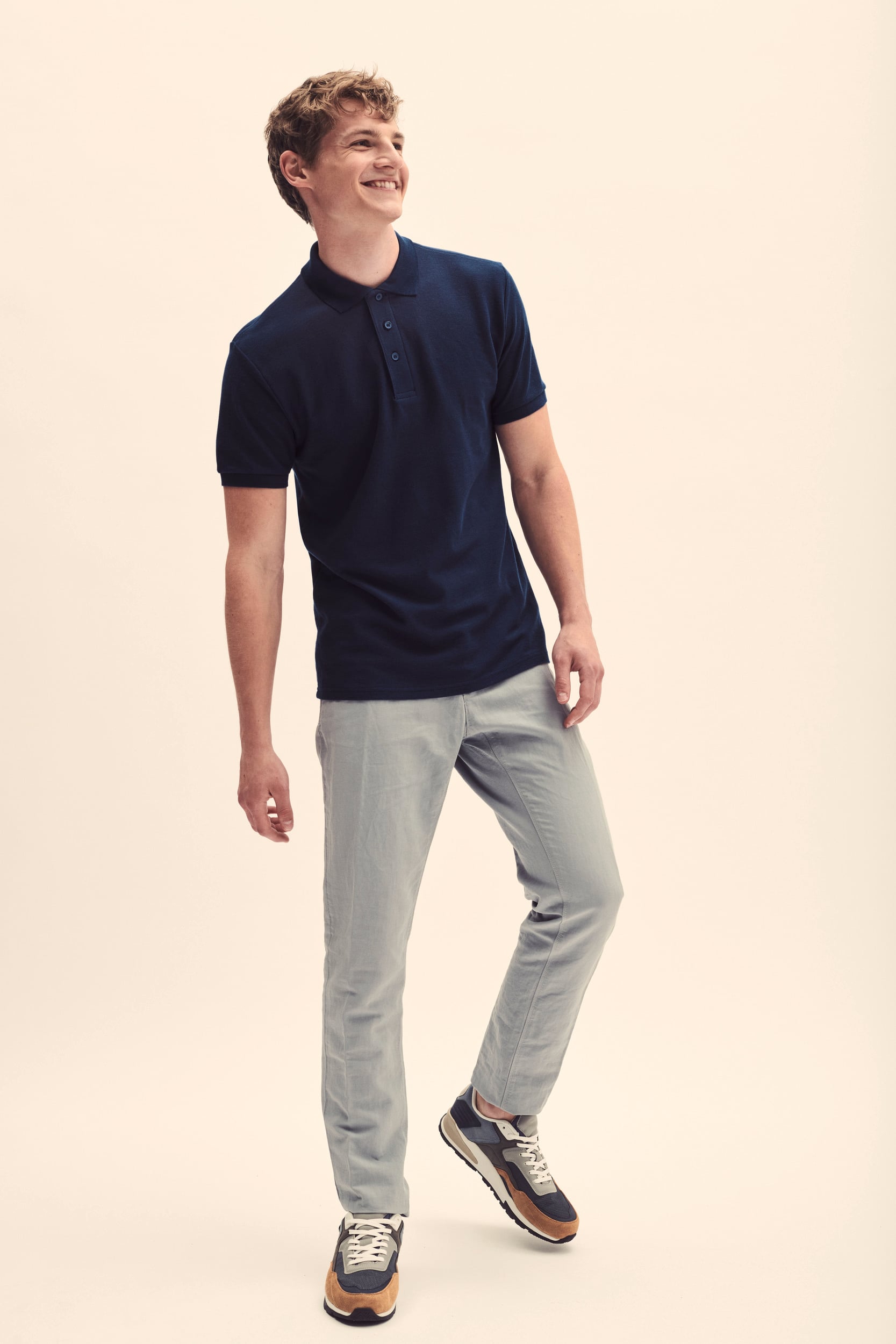 Hombre con polo azul marino de manga corta, pantalones grises y zapatillas deportivas multicolor.