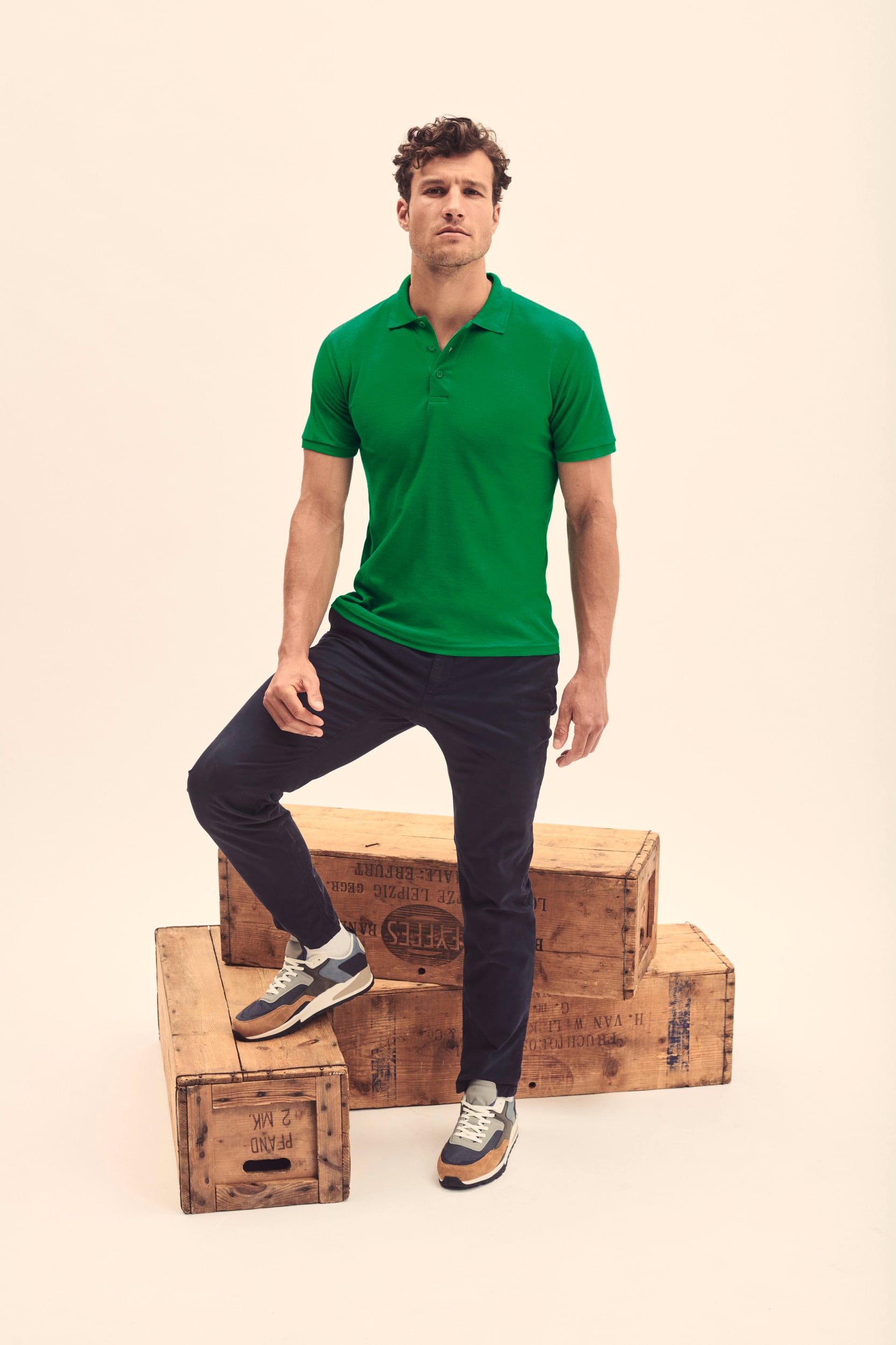 Hombre con polo verde de manga corta y pantalón azul oscuro junto a cajas de madera.