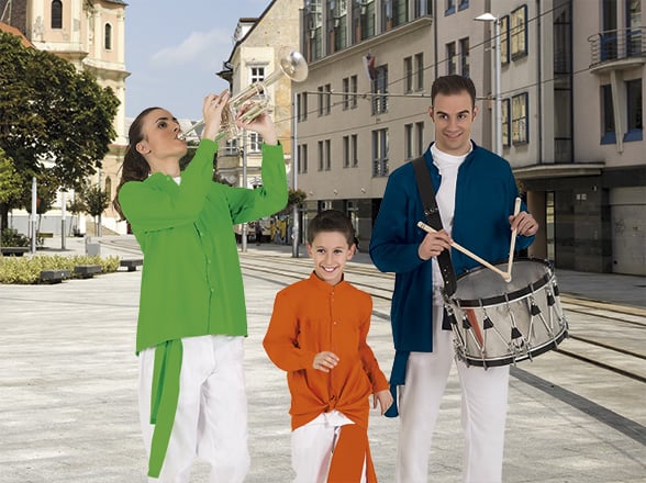 Tres músicos con camisa tradicional de colores verde, naranja y azul tocando trompeta y tambor en una plaza urbana.